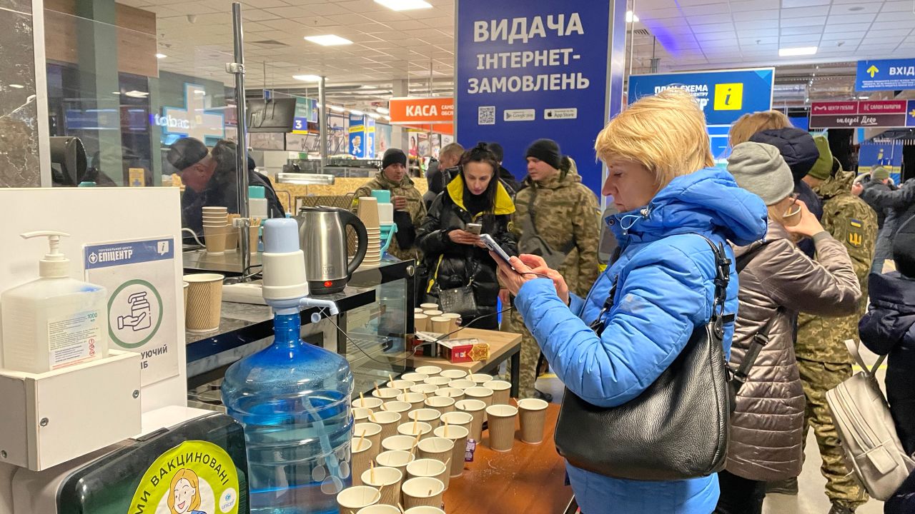 Women receive hot drinks and check their phones in the Epicenter supermarket in Zaporizhzhia, a makeshift processing center for refugees.