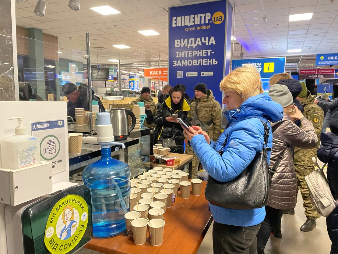 Women receive hot drinks and check their phones in the Epicenter supermarket in Zaporizhzhia, a makeshift processing center for refugees.