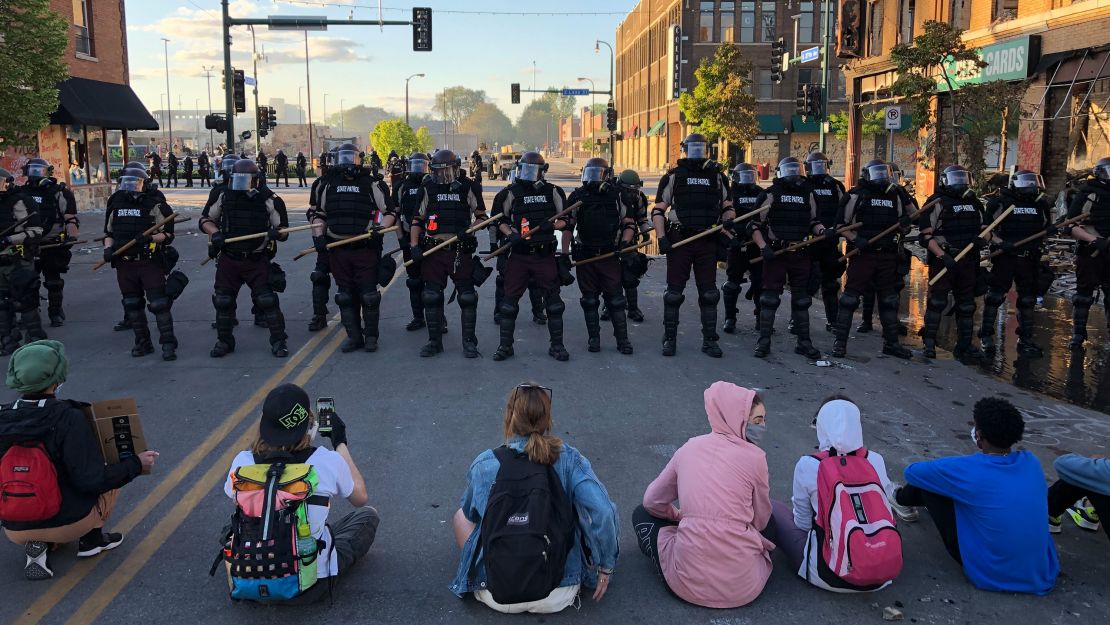 People sit on the street in front of a row of police officers during a rally in Minneapolis, Minnesota, on May 29, 2020 after the death of George Floyd.