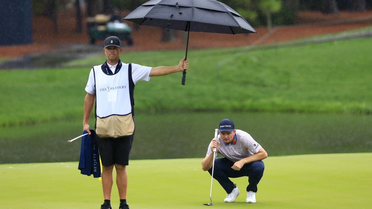 Justin Rose of England lines up a putt as caddie David Clark holds an umbrella.