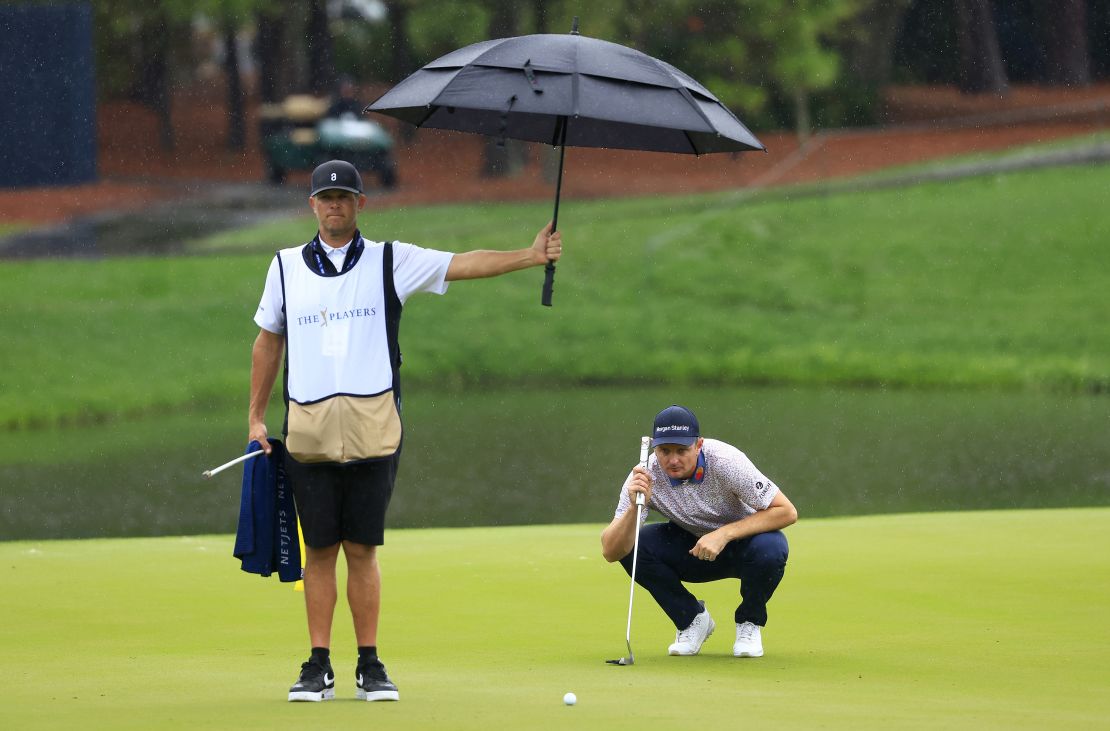 Justin Rose of England lines up a putt as caddie David Clark holds an umbrella.