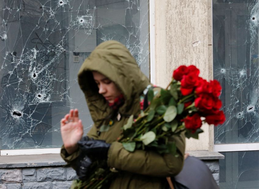 A woman walks past a damaged window to lay flowers at a makeshift memorial for victims in Donetsk, Ukraine, on March 15.
