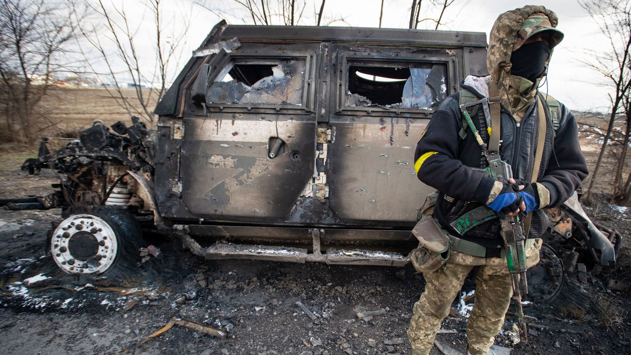 A Ukrainian soldier stands beside a burned out Russian Tigr fighting vehicle.