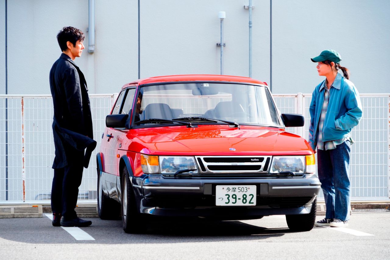 Hidetoshi Nishijima and Toko Miura, as Yusuke Kafuku and Misaki Watari, standing next to the red Saab 900 Turbo in Hamaguchi's "Drive My Car." "I have always felt that it is easy to have a very intimate conversation in a car," the director tells CNN.