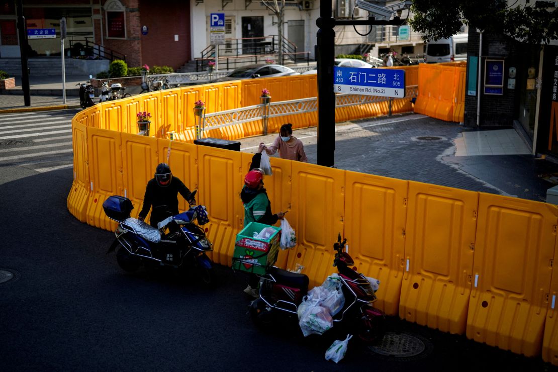 A delivery worker passes food to a woman over the barriers of an area under lockdown in Shanghai on March 23, 2022. 