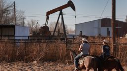 Alejandro Galindo, left, and Sarah Ibarra exercise their horses near an oil pumpjack pulling oil from the Permian Basin oil field on March 13, 2022 in Odessa, Texas. 