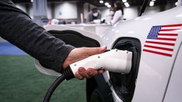 An exhibitor demonstrates plugging in a charging port for a Ford Motor Co. Mustang during the Washington Auto Show in Washington, D.C., U.S., on Friday, Jan. 21, 2022.