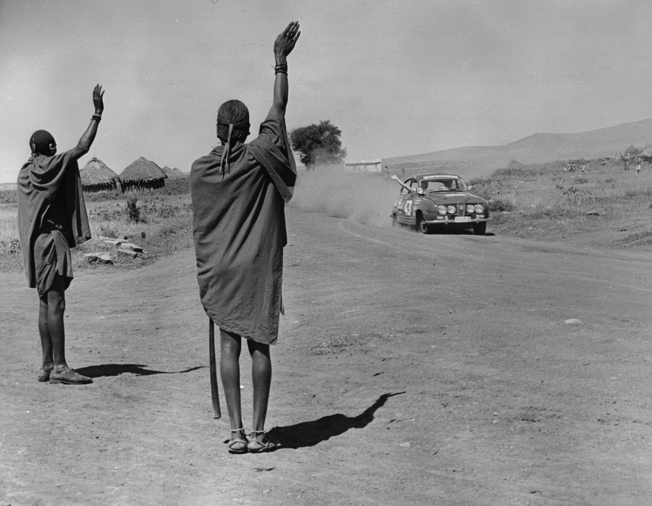 Competitors<strong> </strong>Pat Moss-Carlsson and Elizabeth Nystrom exchange a wave with Maasai onlookers during practice for the 1966 East African Safari Rally.