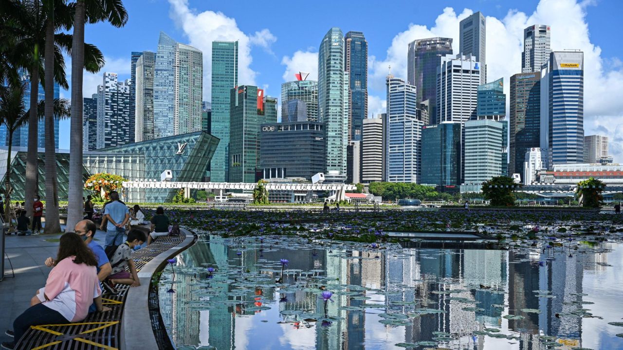 This photograph taken on June 14, 2021 shows people sitting next to a pond with the view of the skyline in Singapore. - A financial exchange offering carbon credits and investments in conservation projects is set to launch in Singapore, but it may struggle to convince sceptics of the value of controversial carbon offsets.  - TO GO WITH Singapore-market-climate, FOCUS by Martin Abbugao and Sam Reeves (Photo by Roslan RAHMAN / AFP) / TO GO WITH Singapore-market-climate, FOCUS by Martin Abbugao and Sam Reeves (Photo by ROSLAN RAHMAN/AFP via Getty Images)