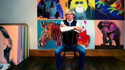 American Pop artist Andy Warhol sits in front of several paintings in his 'Endangered Species' at his studio, the Factory, in Union Square, New York, New York, April 12, 1983.