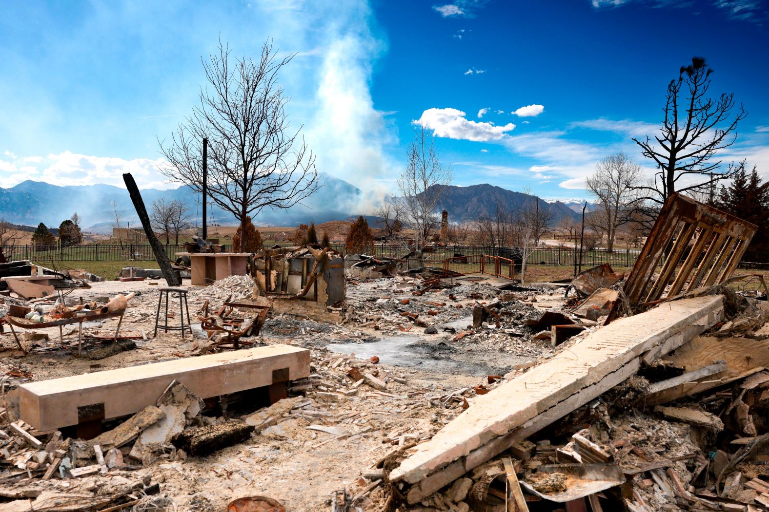 A Boulder home that was destroyed in the Marshall Fire last year sits in ruins as the NCAR Fire burns in the distance on March 26.
