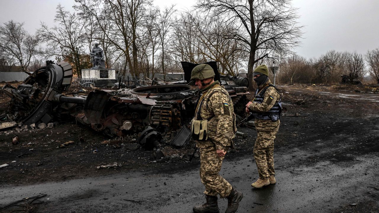 Ukrainian soldiers patrol next to a destroyed Russian tank in the village of Lukianivka near Kyiv on March 30, 2022. 