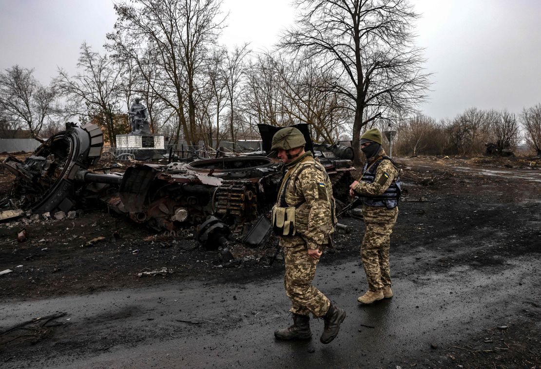 Ukrainian soldiers patrol next to a destroyed Russian tank in the village of Lukianivka near Kyiv on March 30, 2022. 