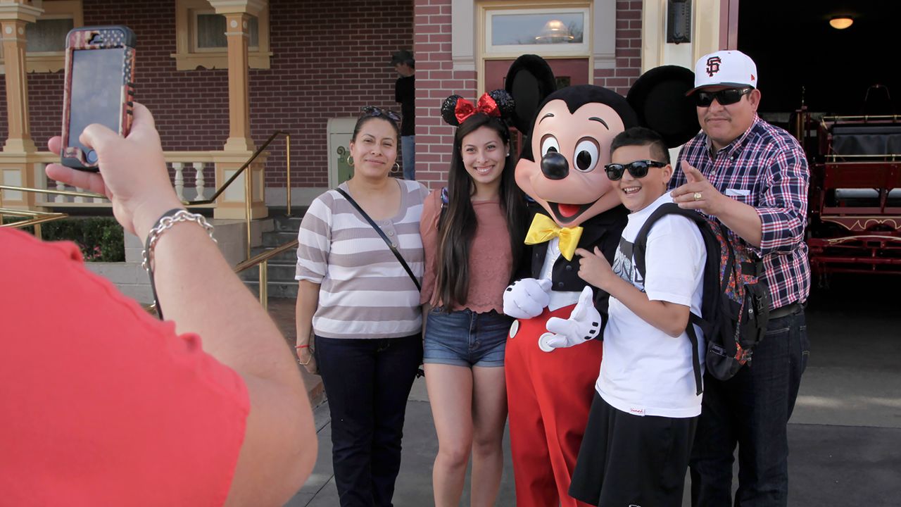 Mickey Mouse poses with visitors at Disneyland, Thursday, Jan. 22, 2015, in Anaheim, Calif. Seventy people have been infected in a measles outbreak that led California public health officials to urge those who haven't been vaccinated against the disease, including children too young to be immunized, should avoid Disney parks where the spread originated. (AP Photo/Jae C. Hong)