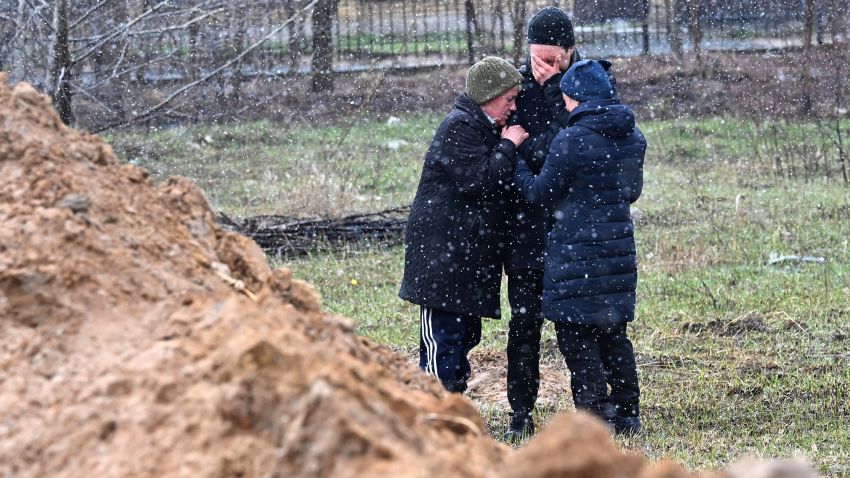 People react as they gather close to a mass grave in town of Bucha, just northwest of the Ukrainian capital Kyiv on April 3, 2022. 