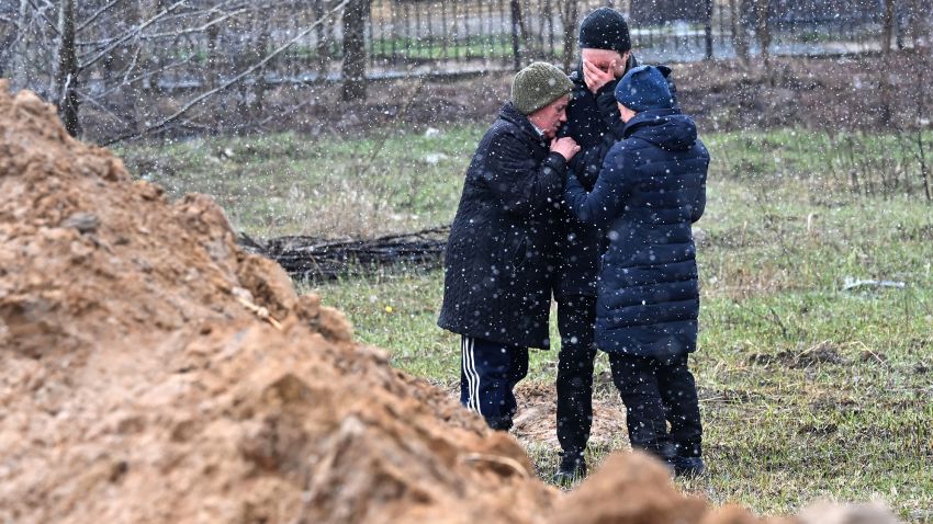 People react as they gather close to a mass grave in town of Bucha, just northwest of the Ukrainian capital Kyiv on April 3, 2022.