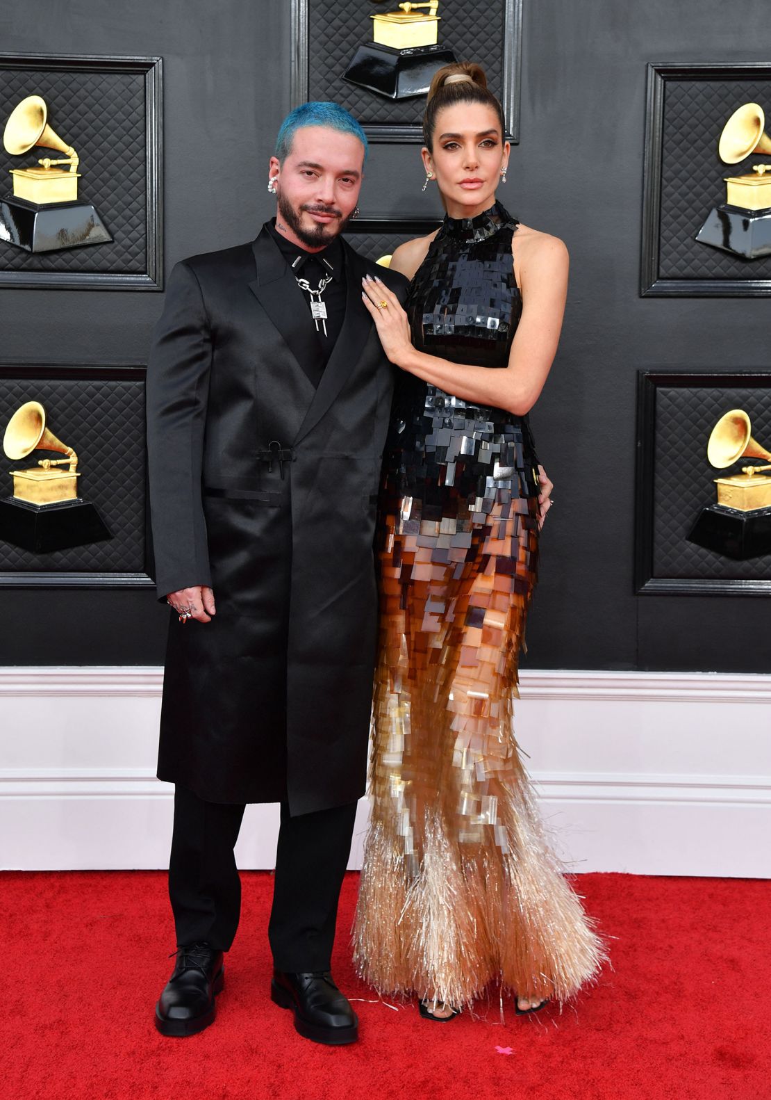 J Balvin elevated the suit silhouette in a tailored knee-length coat, while model Valentina Ferrer opted for a high-neck layered ombre dress with a gold fringed hem. 