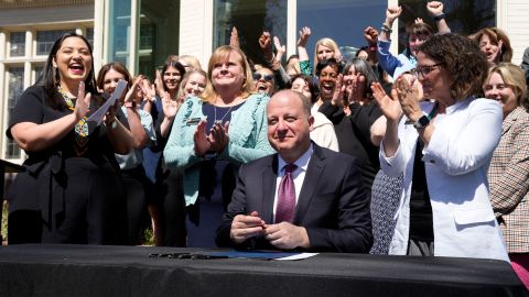 Colorado Gov. Jared Polis, front, signs into law the Reproductive Health Equity Act during a ceremony outside the governor's mansion on Monday, April 4, 2022, in Denver.