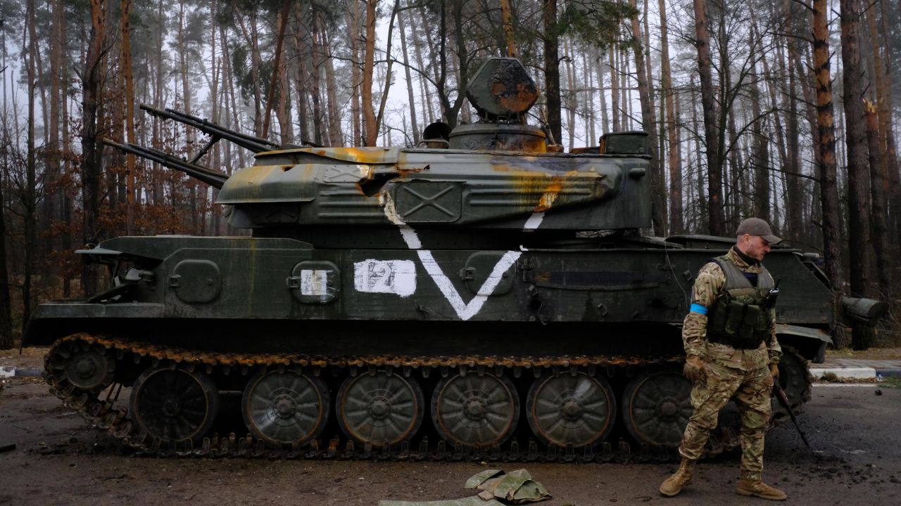 A member of the Ukrainian Territorial Defense forces inspects a destroyed Russian armored vehicle on the E-40 highway.