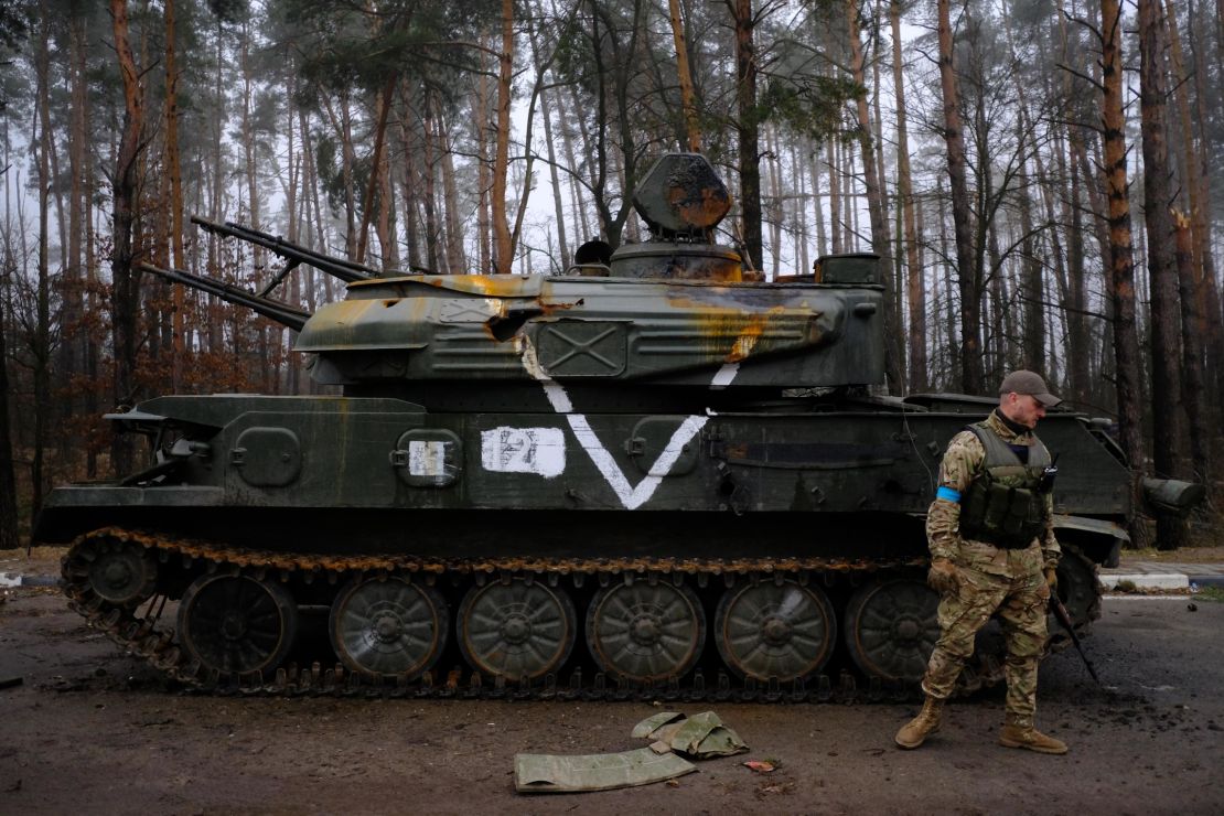 A member of the Ukrainian Territorial Defense forces inspects a destroyed Russian armored vehicle on the E-40 highway.