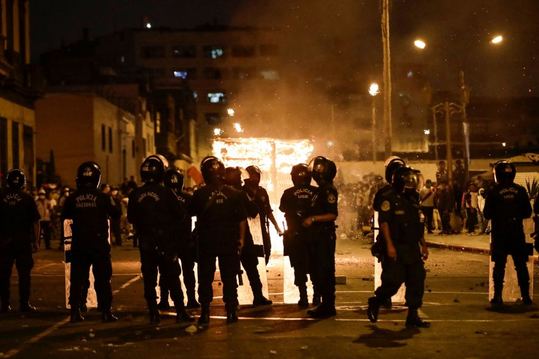 Police officers in Lima stand in front of a burning street vendor structure during a demonstration against Peruvian President Pedro Castillo. The protests began over rising fuel and fertilizer prices triggered by the Ukraine conflict, but have expanded in scope.