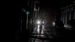 A cars headlights are seen past people walking on a dark in San Juan, Puerto Rico after a major power outage hit the island on April 6, 2022. (Photo by Ricardo ARDUENGO / AFP) (Photo by RICARDO ARDUENGO/AFP via Getty Images)