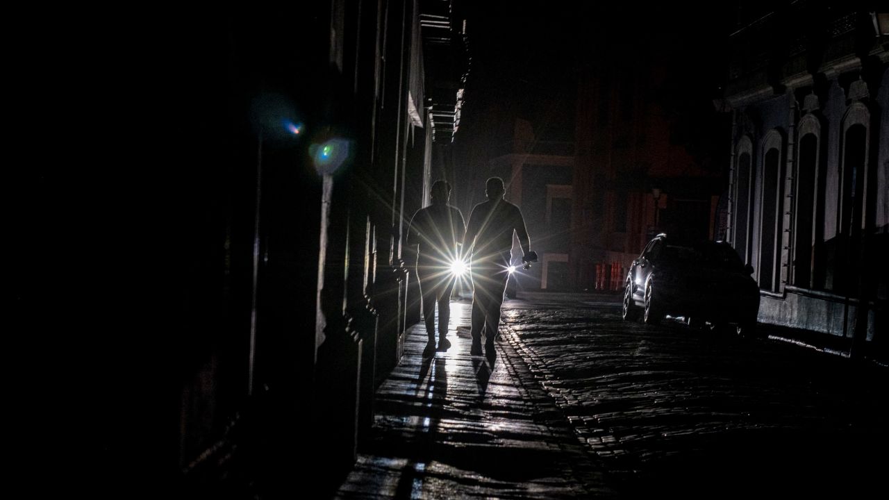 A vehicle's headlights illuminate people walking on a dark street in San Juan, Puerto Rico, after a power outage on the island Wednesday. 