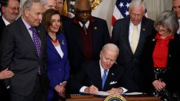 WASHINGTON, DC - APRIL 06: U.S. President Joe Biden (C) signs the Postal Service Reform Act into law during an event with (L-R) Sen. Gary Peters (D-MI), Senate Majority Leader Charles Schumer (D-NY), Speaker of the House Nancy Pelosi (D-CA), House Majority Whip James Clyburn (D-SC), House Majority Leader Steny Hoyer (D-MD) and retired letter carrier Annette Taylor and others in the State Dining Room at the White House on April 6, 2022 in Washington, DC. A part of Postmaster General Louis DeJoy's controversial 10-year restructuring plan, the law provides $107 billion to modernize and streamline the long-beleaguered Postal Service. (Photo by Chip Somodevilla/Getty Images)