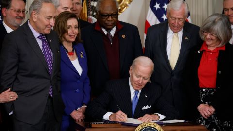 President Joe Biden signs the Postal Service Reform Act into law during an event with (from left) Sen. Gary Peters (D-MI), Senate Majority Leader Charles Schumer (D-NY), Speaker of the House Nancy Pelosi (D-CA), House Majority Whip James Clyburn (D-SC), House Majority Leader Steny Hoyer (D-MD) and retired letter carrier Annette Taylor and others in the State Dining Room at the White House on Wednesday, April 6, 2022, in Washington. 