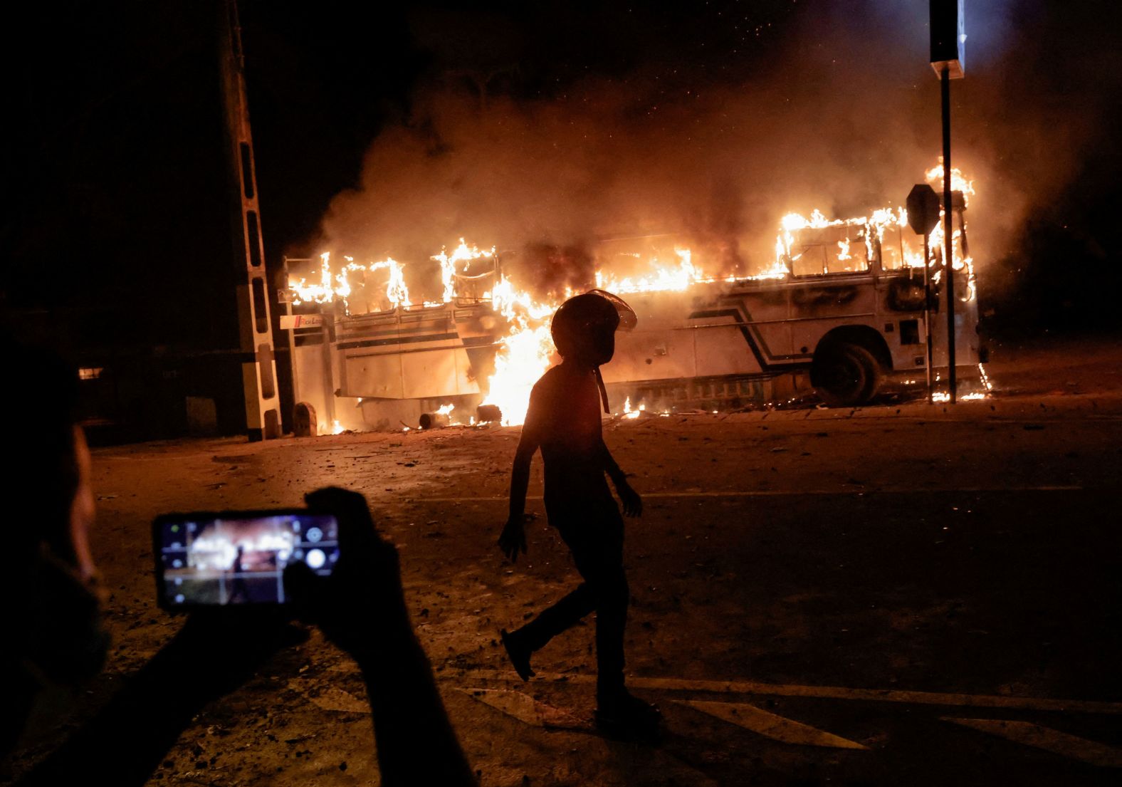 A person takes a photo as a demonstrator walks near a bus that was set on fire outside the home of Sri Lankan President Gotabaya Rajapaksa on Thursday, March 31. Rajapaksa <a href="index.php?page=&url=https%3A%2F%2Fwww.cnn.com%2F2022%2F04%2F01%2Fasia%2Fsri-lanka-state-of-emergency-protests-intl-hnk%2Findex.html" target="_blank">declared a nationwide state of emergency</a> following the violent protests. The island nation of 22 million people is struggling with its worst economic crisis in decades.