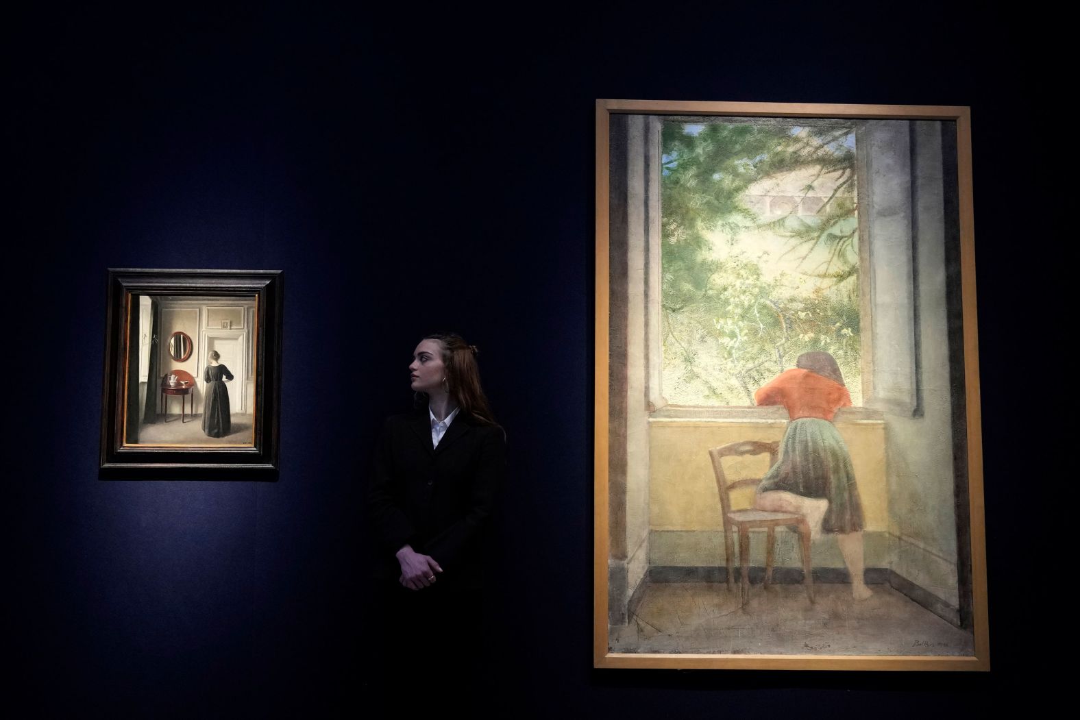 An employee of the Christie's auction house in London looks at Vilhelm Hammershoi's painting "An Interior with an Oval Mirror," left, next to Balthus' painting "Jeune fille à la fenêtre" on Tuesday, April 5. Both are expected to fetch millions.