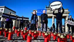 08 April 2022, Berlin: Activists wearing masks with the likenesses of Chancellor Scholz (M), Finance Minister Lindner (l) and Economics Minister Habeck and holding a sign reading "Oil embargo?" demonstrate at the Brandenburg Gate in favor of an embargo on Russian oil and gas. 