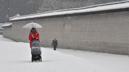 A woman wheels a pushchair along a snow-covered street in central Seoul on January 19, 2022. 