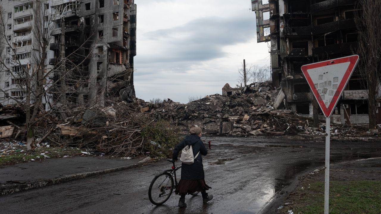 A woman pushes her bicycle in front of a destroyed apartment building in Borodianka, in April 2022.