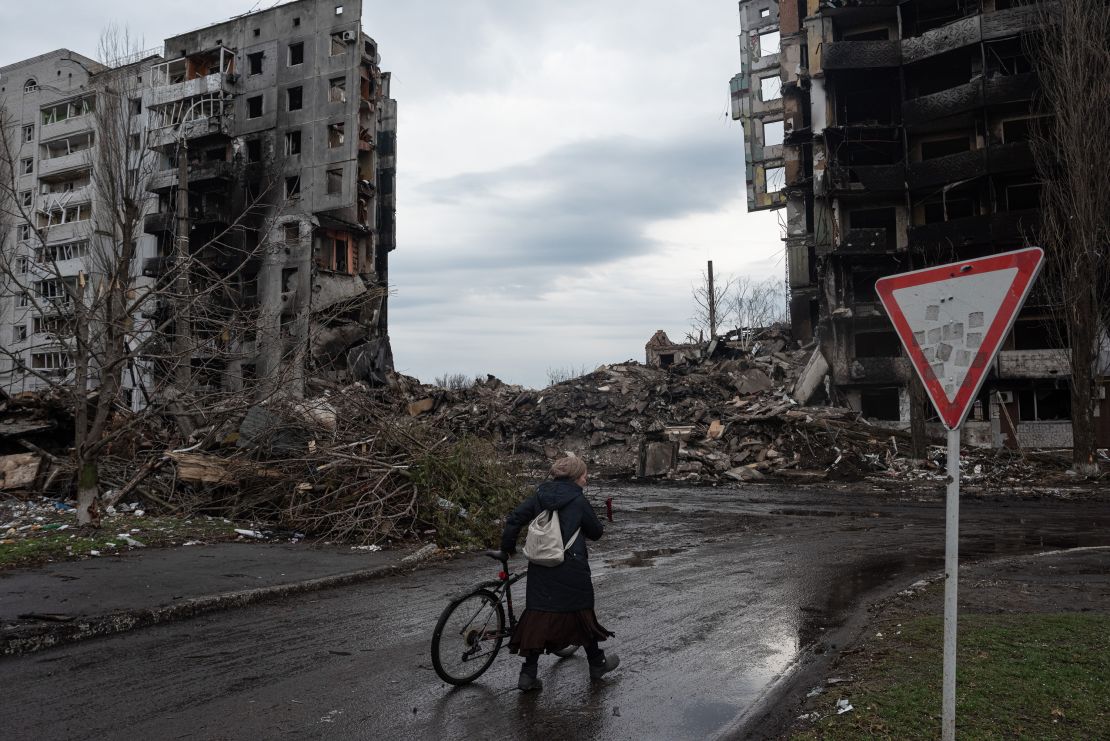 A woman pushes her bicycle in front of a destroyed apartment building in Borodianka, in April 2022.