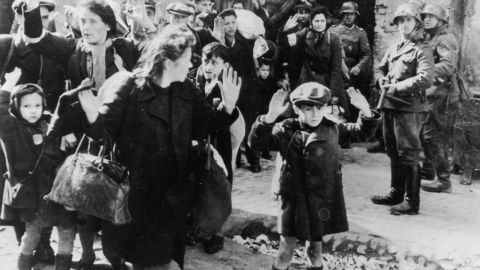 This 1943 photograph, from an official SS report, shows Jewish civilians held at gunpoint by Nazi SS troops after being forced out of a bunker where they were sheltering during the Warsaw Ghetto Uprising.