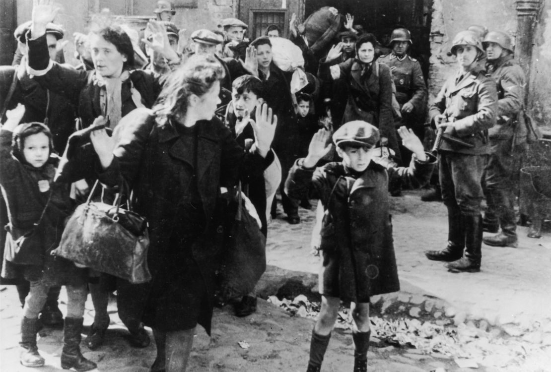 This 1943 photograph, from an official SS report, shows Jewish civilians held at gunpoint by Nazi SS troops after being forced out of a bunker where they were sheltering during the Warsaw Ghetto Uprising.