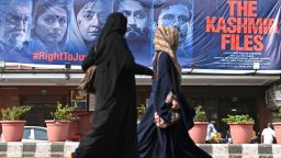 Women walk past a banner of Bollywood movie 'The Kashmir Files' outside a cinema hall in the old quarters of Delhi on March 21, 2022. 