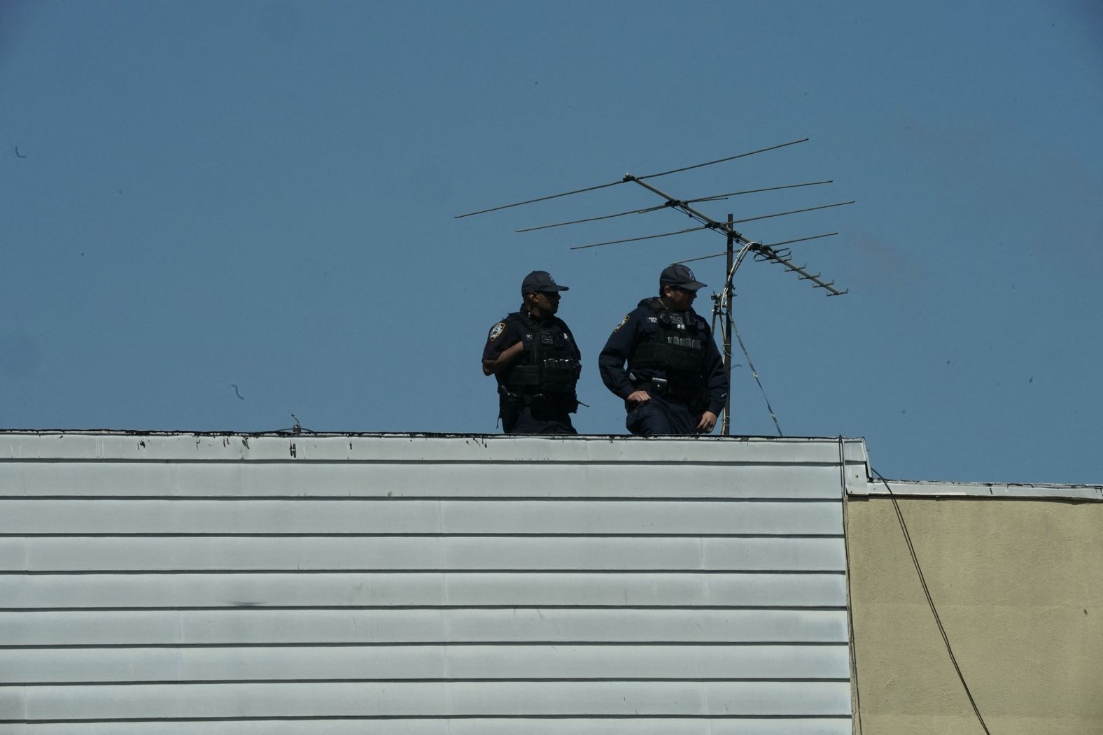 New York City police officers look down from a rooftop.