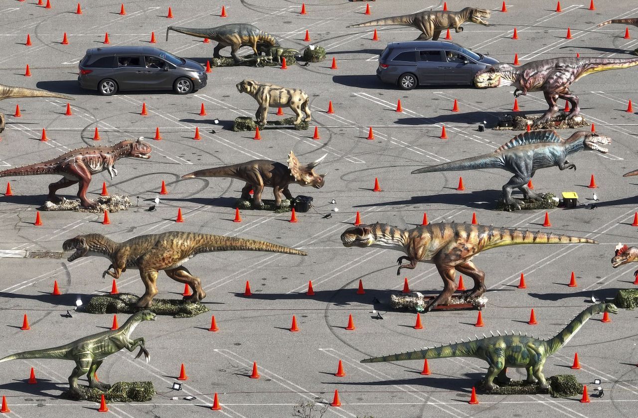 People drive through the parking lot of the Westminster Mall in Westminster, California, on Friday, April 8. More than 30 animatronic dinosaurs were set up along the east side of the mall as part of the Jurassic Empire drive-thru exhibit.