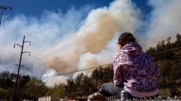 Hope Misquez sits on a fence and watches the McBride Fire from a park in Ruidoso, New Mexico, Wednesday, April 13, 2022. Misquez says her father and friends are helping to fight the fire.