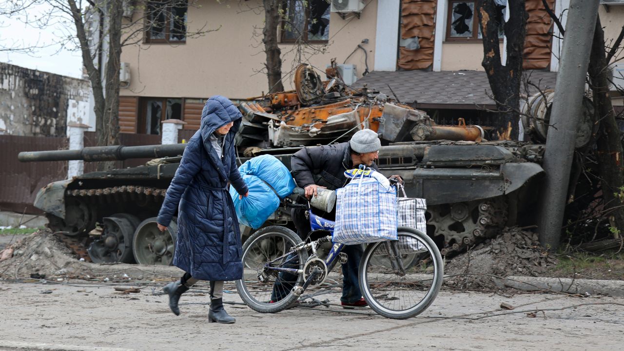 Local civilians walk past a tank destroyed during heavy fighting in Mariupol on April 19.