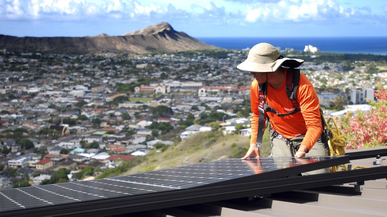 Dane Hew Len, lead installer for RevoluSun, places a solar panel on a roof in Honolulu.