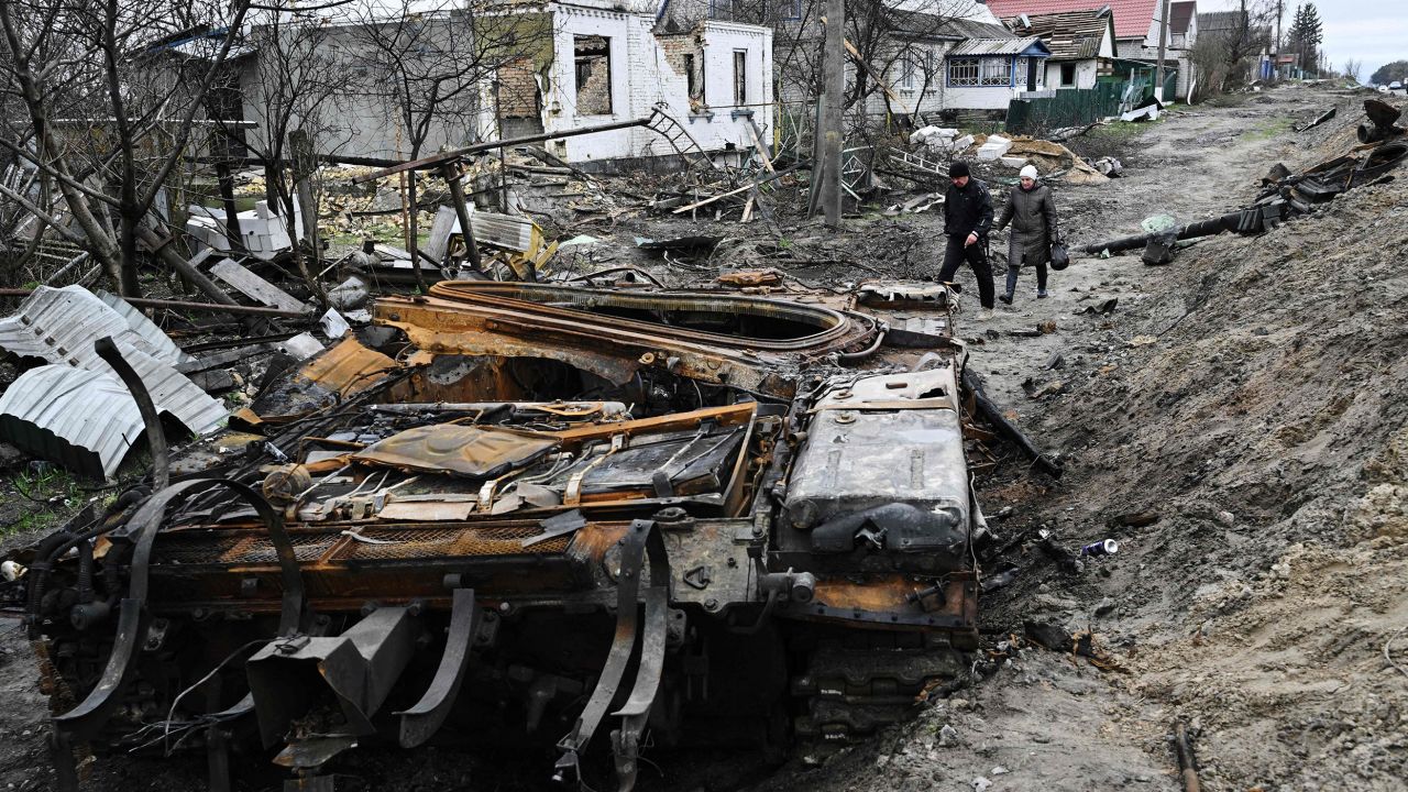 TOPSHOT - Local residents walk amid debris of a charred Russian tank next to destroyed houses in the village of Zalissya, northeast of Kyiv, on April 19, 2022, during the Russian invasion of Ukraine.