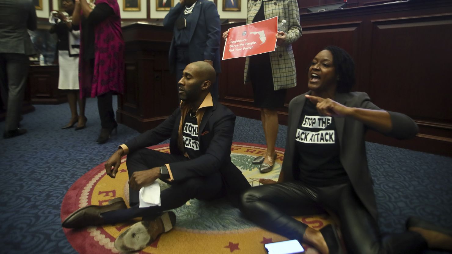 Rep. Tray McCurdy, D-Orlando and Rep. Angie Nixon, D-Jacksonville sit on the Florida Seal in protest as debate stops on Senate Bill 2-C: Establishing the Congressional Districts of the State in the House of Representatives Thursday, April 21, 2022 at the Capitol in Tallahassee, Fla.