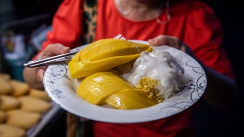 BANGKOK, THAILAND - APRIL 21: A customer holds a plate of mango sticky rice at a night market on April 21, 2022 in Bangkok, Thailand. Mango sticky rice sales have skyrocketed in Bangkok since Milli, a 19-year old Thai rapper, ate the national dish during her performance at the Coachella music festival in California. Milli, the first Thai national to perform solo at the festival, has brought fame to the dish, leaving local mango sticky rice hot spots such as Aunt Lek and Aunt Yai's Mango Sticky Rice in Chinatown and Mae Varee Mango Sticky Rice on Thonglor struggling to keep up with the influx of orders. Thailand hopes that the international attention on the dish will push it to be listed on UNESCO's intangible cultural heritage list. (Photo by Lauren DeCicca/Getty Images)