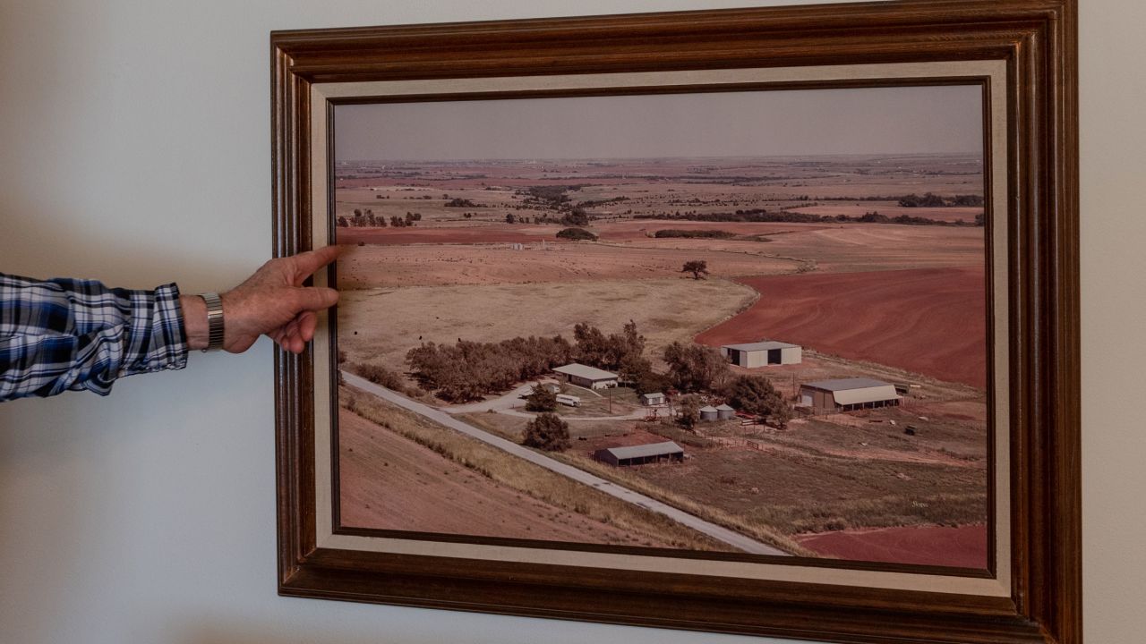 Terry Baker points to a photograph hanging on the wall of Cathy Baker's childhood home showing the family farm in the late 1900s.