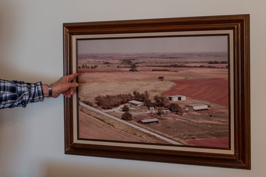 Terry Baker points to a photograph hanging on the wall of Cathy Baker's childhood home showing the family farm in the late 1900s.