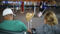 A hat rests on a luggage handle as travelers sit in a waiting area at Rhode Island T.F. Green International Airport in Providence, R.I., Tuesday, April 19, 2022. 
