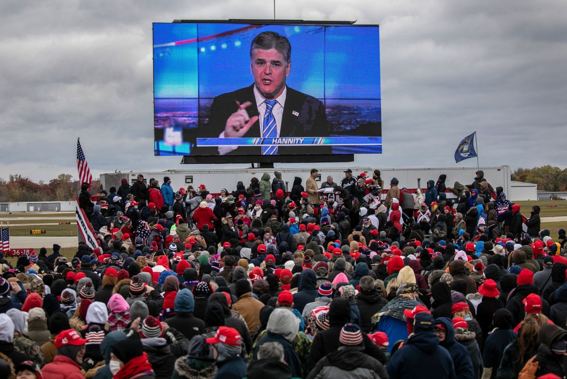 Supporters of U.S. President Donald Trump watch a video featuring Fox host Sean Hannity ahead of Trump's arrival to a campaign rally in Michigan on October 30, 2020.